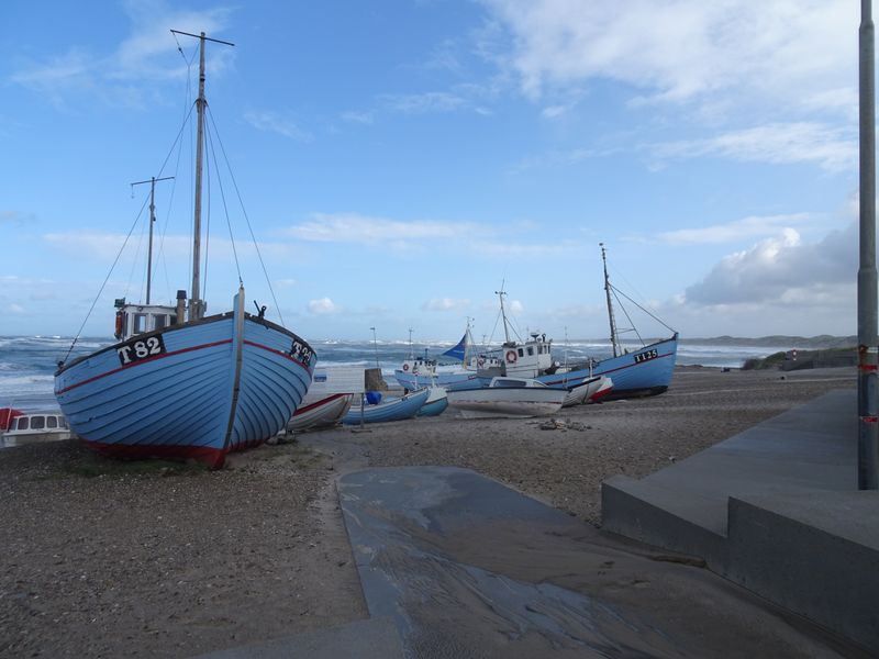 Blauwe vissersboten op het strand, met hoge golven op zee erachter