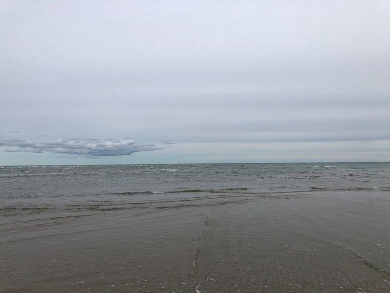 Grijze zee onder een grijze lucht en een natte zandbank