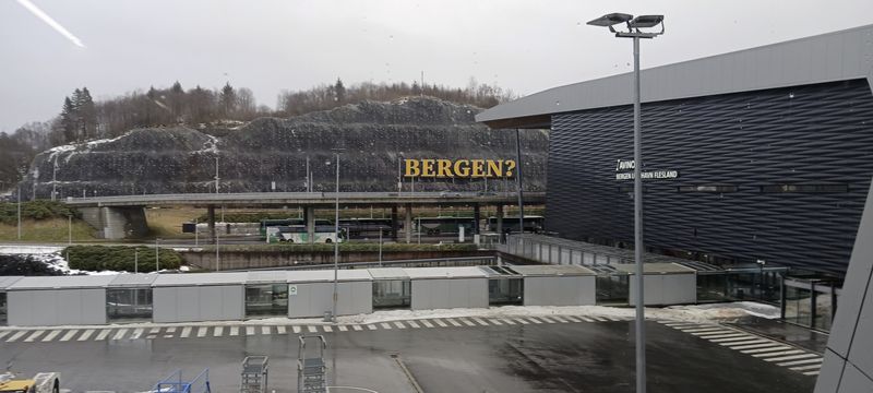 Een rotswand met het gele opschrift Bergen met een vraagteken, naast de luchthaven van Bergen