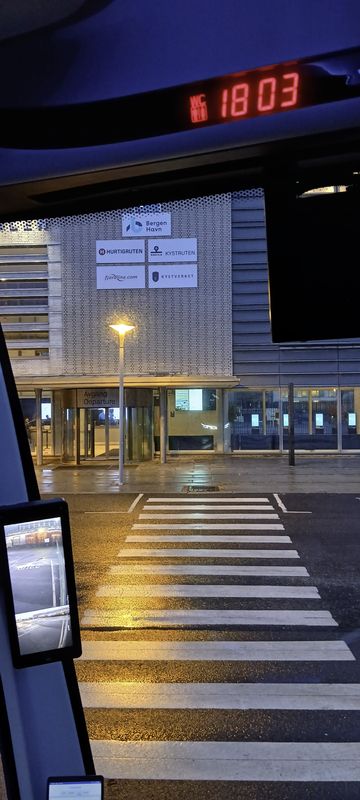 Uitzicht door een busraam op de terminal van Bergen Havn met borden van onder meer Hurtigruten