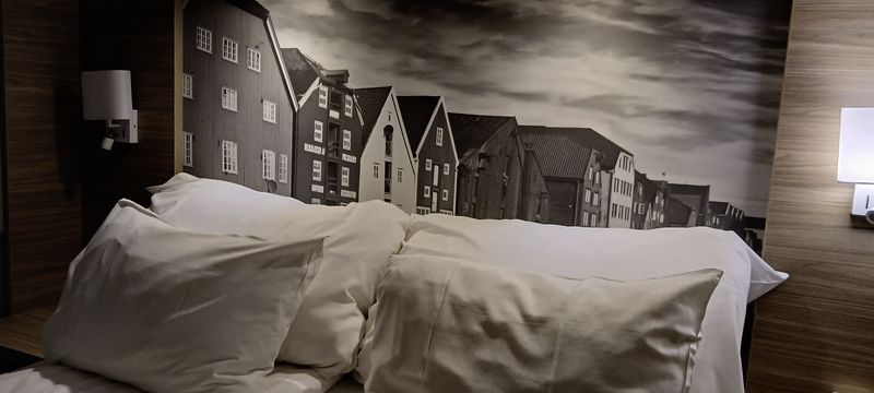 Een opgemaakt bed in de hut met een zwart-wit foto van oude houten pakhuizen aan het hoofdeinde