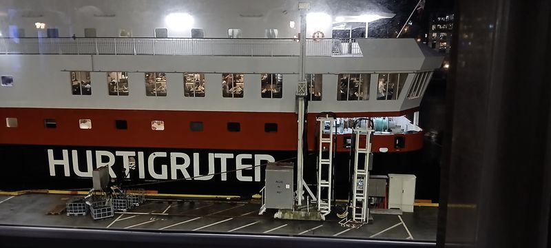 Een Hurtigruten-schip aan de kade in de avond, met verlichte eetzaal